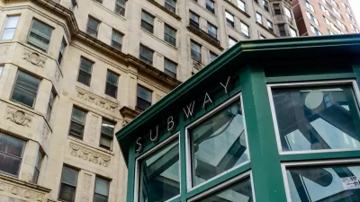 Green subway station entrance kiosk with brick buildings in background.