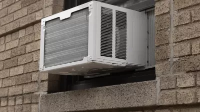 Close-up of white air conditioning window unit in window of brown brick building.