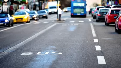 Close-up of white BUS letters on asphalt bus lane with blurred bus and traffic in background.
