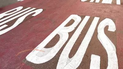 White BUS ONLY letters on red painted bus lane on street.