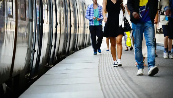 Low shot of side of subway or commuter train and passengers walking on platform next to it.