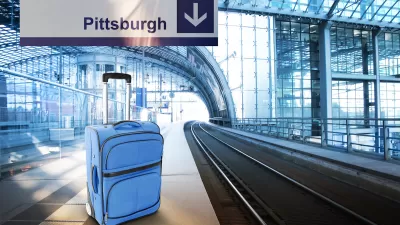 Blue suitcase sits on empty train platform with sign above labeled "Pittsburgh."