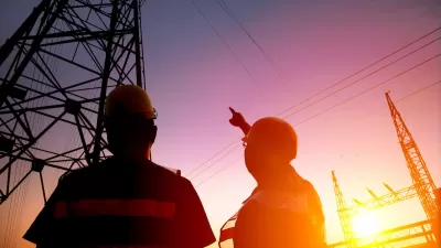 Two utility workers looking up at power lines against purplish sunset sky.