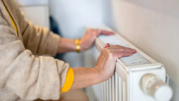 Close-up of older woman's hands resting on white modern heating radiator mounted on wall indoors.