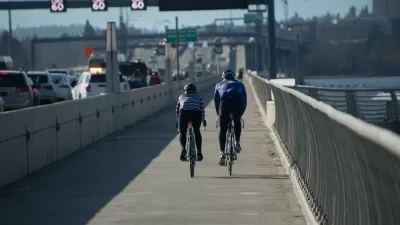 Two cyclists riding on a protected bike lane on a bridge in Seattle with traffic on their left.