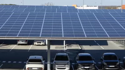 Solar panels installed as shade panels over parking lot with small cars parked underneath.