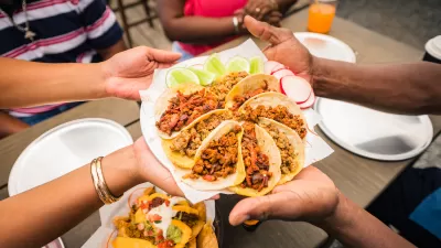 Close-up of multiple hands holding up plate of street-style tacos arranged in circular shape.
