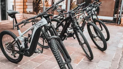 Black e-bikes sitting on a sidewalk outdoors.