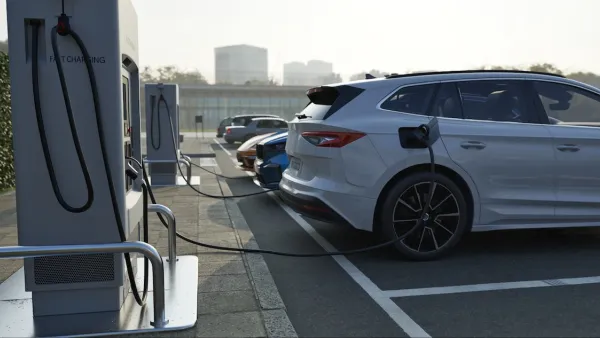 Row of vehicles parked and plugged in at EV charging station.