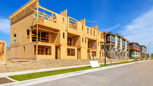 Wood-frame multifamily housing units under construction on a street in low-density area or suburb.