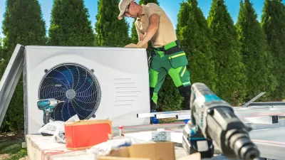 HVAC technician on roof installing heat pump with tools in foreground.