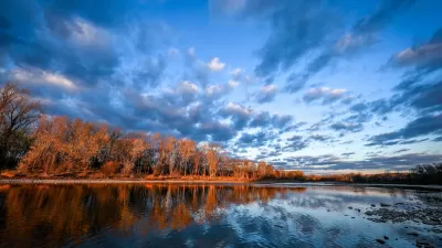 View of calm Maumee River with fall foliage on other side at sunset.