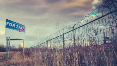 Fence with barbed wire and For Sale sign around vacant field.