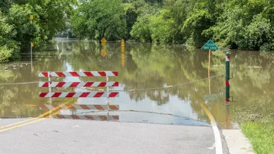 Flooded road with red and white gate barrier blocking entry in Houston, Texas.