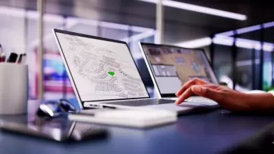 Close-up of laptop with GIS parcel map open and hand resting on keyboard in modern office.