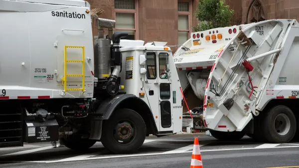 Two white garbage trucks stopped on New York City street.