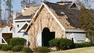 Front view of stone home with severe tornado damage and portions of roof ripped off.