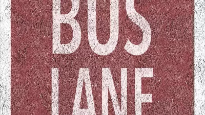 Overhead view of white BUS LANE sign painted on red background on concrete street.