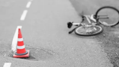 Blurred black and white image of bicycle laying down in road with orange traffic cone in foreground.