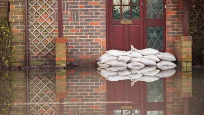 Sandbags stacked in front of a red door on a brick building with ground in front flooded with water