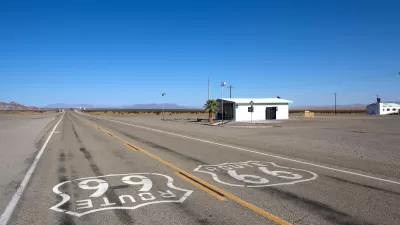 Low shot of Route 66 signs on asphalt with small abandoned building on roadside on old Route 66 near Amboy, California.