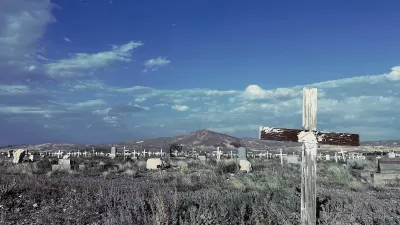 Old cemetery with weathered wooden cross grave markers in Goldfield, Nevada with mountain in background and blue sky.