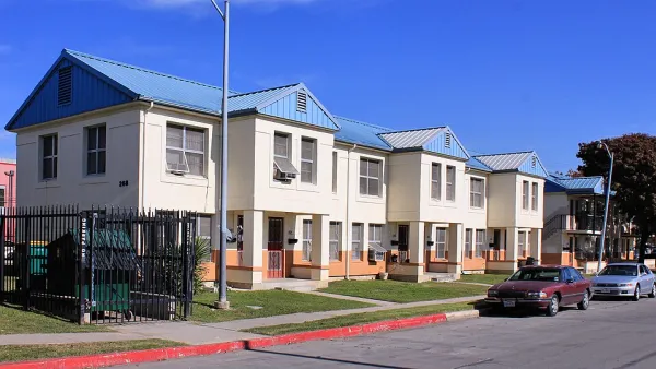 A row of tan homes with blue roofs along a road.
