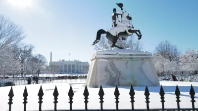 A snow covered statue looks out over a blanket of snow at the White House, which is also covered in snow.