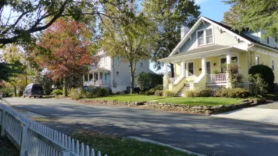 Large historic homes and white picket fences line a street.