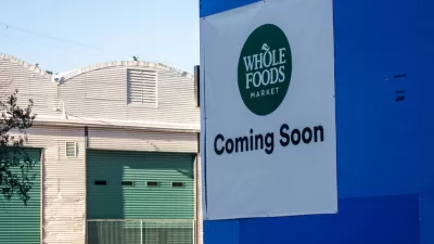 Austin, TA sign reading "Whole Foods Coming Soon" adorns a blue wall across the street from warehouses.