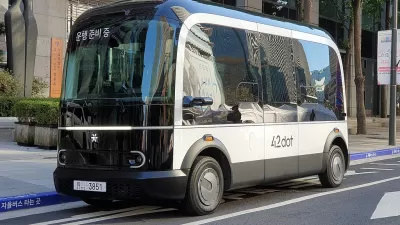 A small boxy driverless shuttle pulled up to a curb.