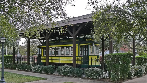 Yellow vintage Houston streetcar labeled Bellaire parked on display under covered carport surrounded by wrought iron fence in Houston, Texas.