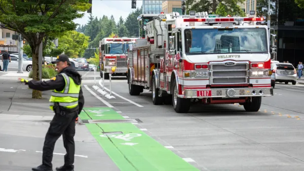 A police officer directs traffic as fire trucks arrive on scene along a street with green painted bike lanes.