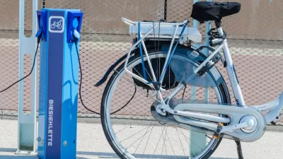 An e-bike is plugged into a public charger on a sunny day.