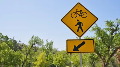 A yellow sign points to a bike and pedestrian path with open park space in the background.