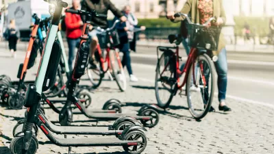 Parked electric scooters on a sidewalk with person walking bike in the background