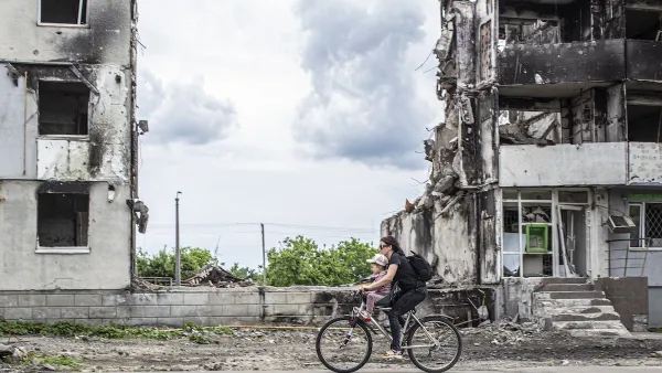 Woman and child ride bike past war-destroyed buildings in Borodyanka, Ukraine.