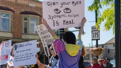 A Black LIves Matter Protest, with a protestor holding up a sign that reads "Open Your Eyes: Systemic Racism Is Real"