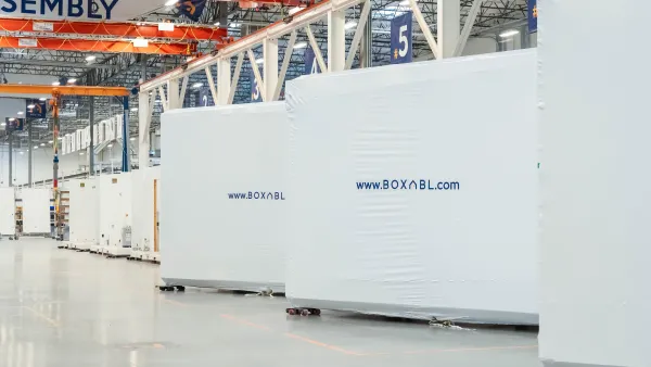 Line of modular tiny home materials wrapped in white tarp with Boxabl logo on each box in warehouse/factory.