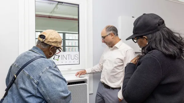 Two Black women and a white man look at a window equipped heat pump in the showroom apartment.