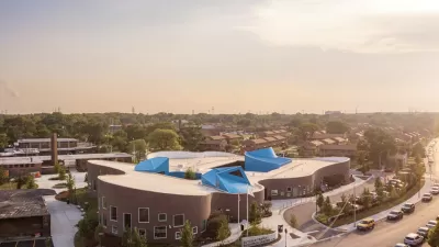 A large, multi-use building is adorned with blue canopies, pictured in the sunset of an urban landscape.