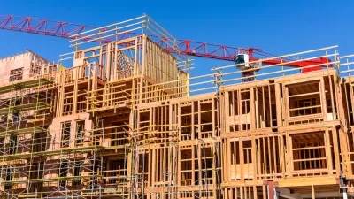 Wood-framed apartment building under construction with red crane in background