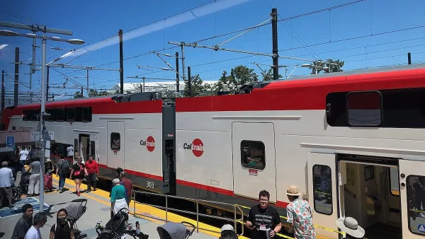 White and red Caltrain electric train at platform with people walking around.