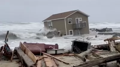 A house has been swept into the Atlantic Ocean by high tides, leaving ruins in onshore as the house appears half submerged by water,