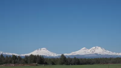 The Three Sisters, snow-covered mountains in Central Oregon, are visible in the distance beyond a farm.