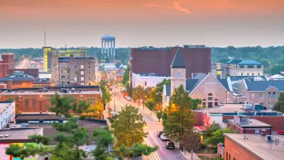 A small town in the U.S. Midwest at dusk, with cars parked on a street lined with historic buildings and a water tower in the distance.