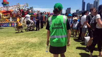 A person in a bright green vest with the words "Covid Marshall" patrols a street fair in Australia.