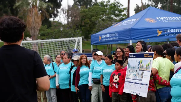 Crowd at event unveiling MacArthur Park transformation project standing next to display board with renderings.