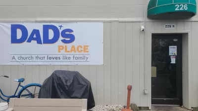 White sign on side of tan building with metal siding and green overhang, reading "Dad's Place, a church that loves like family."