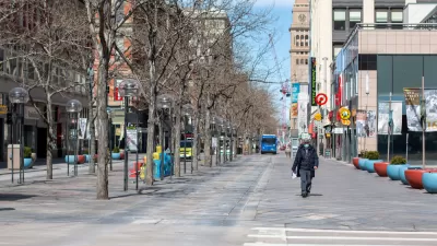 One man, wearing a mask, walks down an otherwise empty 16th St in Denver.